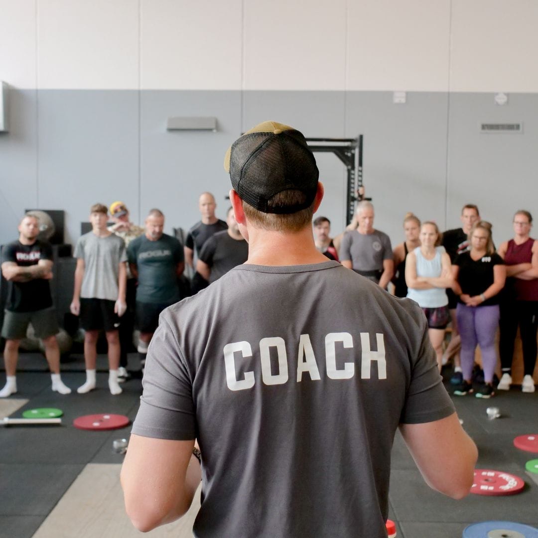 Coach begeleidt cliënt bij persoonlijke training in CrossFit-gym voor op maat gemaakte gezondheidsdoelen.